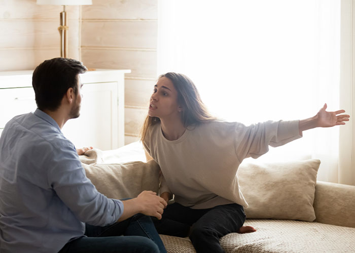Couple having intense discussion on couch, illustrating conflict about tattoo of late son's name and emotional triggers.