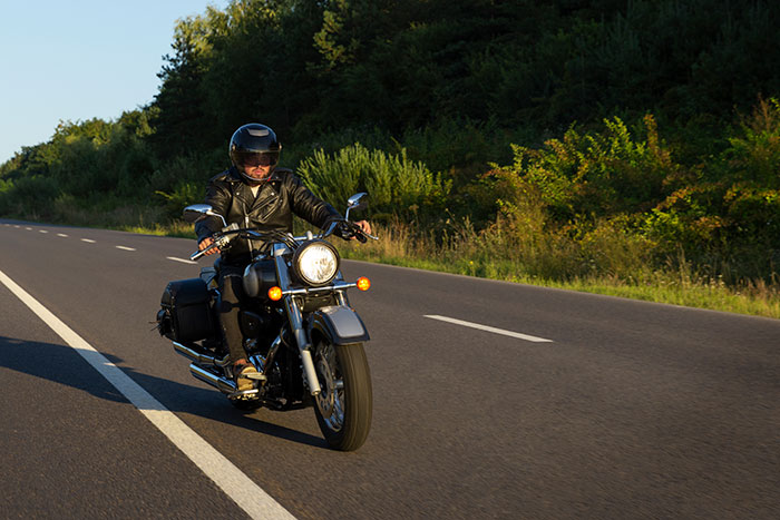 Man riding a motorcycle on an open road, wearing a helmet and leather jacket, enjoying time with pals outdoors.