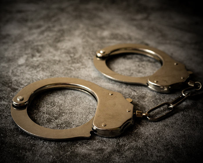 Silver handcuffs on a dark textured surface symbolizing a Batman villain turning himself in for homicide.