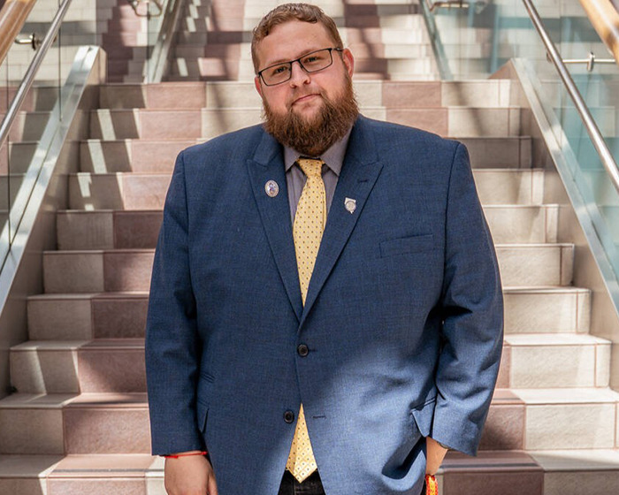 Man with beard and glasses in a blue suit standing on stairs, revealing plans if brother's biological father is confirmed.
