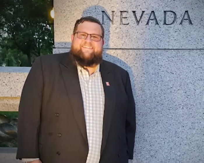 Man with glasses and beard smiling near a Nevada monument, linked to story about biological father and family accusations.