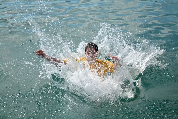 Child in a yellow shirt joyfully splashing in water, capturing moments of good news and positive energy.