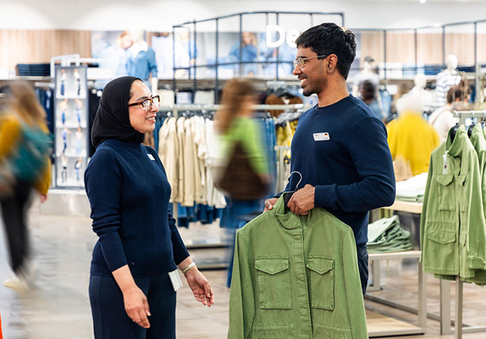 Retail employee in store assisting customer with green jacket, highlighting alleged trans employee customer interaction.