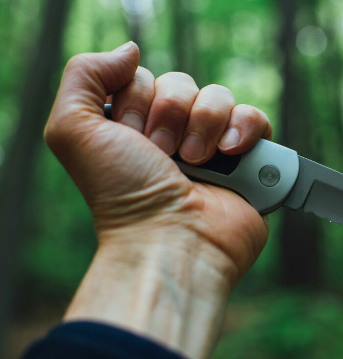 Hand gripping a knife outdoors in a forest, evoking creepy and unsettling feelings from Reddit encounters.