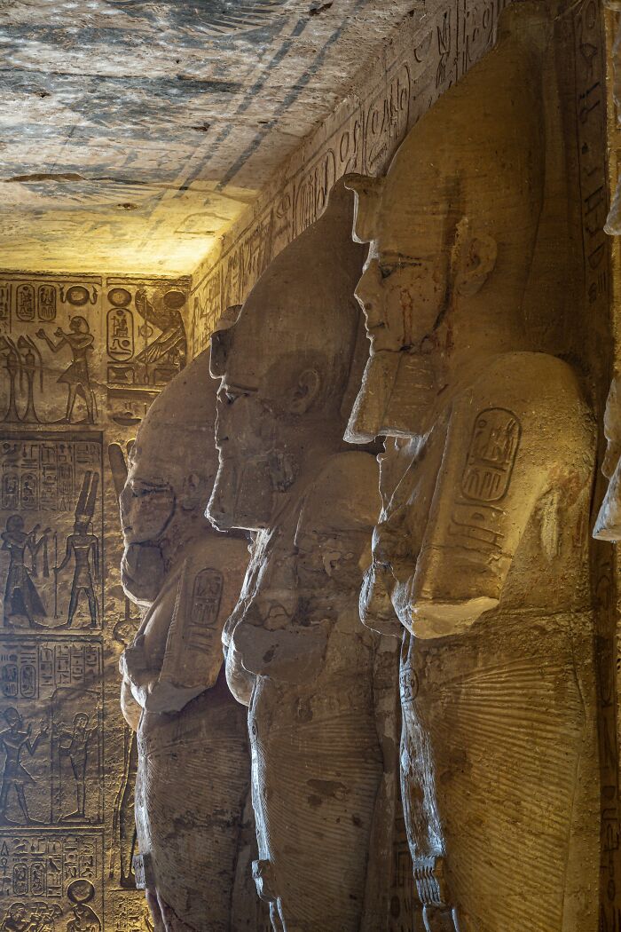 Ancient Egyptian statues with hieroglyphs on walls in a dimly lit historic temple interior.