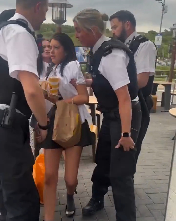 Police officers escort teenage girl outside McDonald's during mass debate over two tier policy banning school kids.