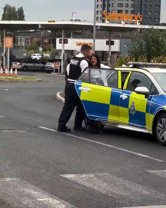 Police officer escorting a woman into a police car outside a Sainsbury's, relating to two tier mass debate over school kids policy.