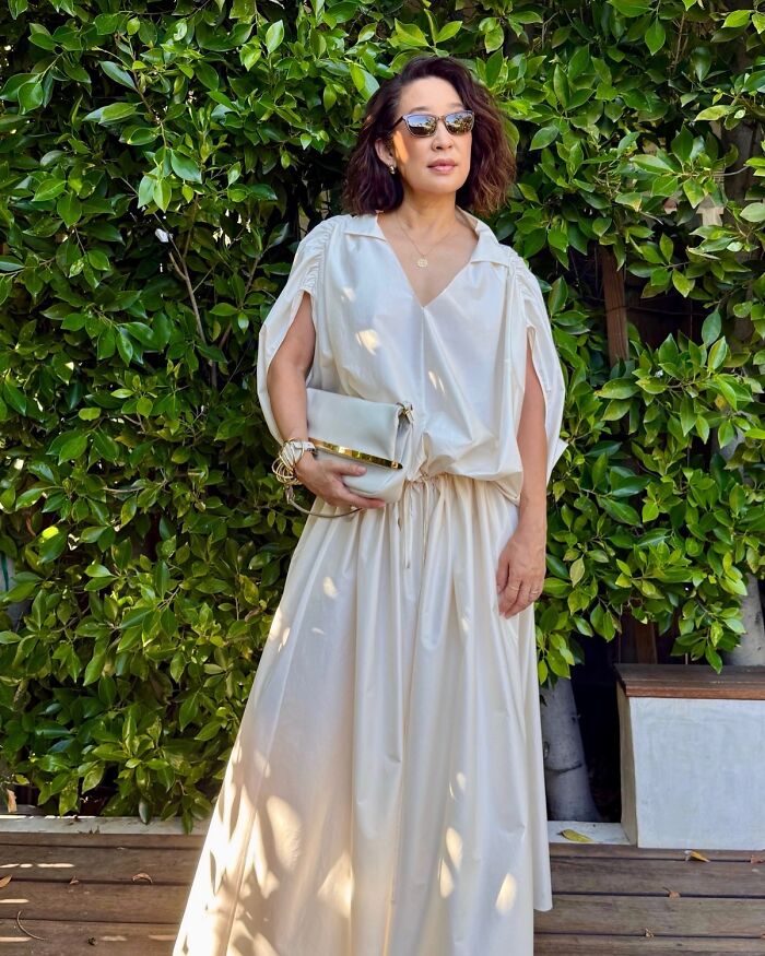 Woman wearing sunglasses and a flowing cream dress standing outdoors with greenery, relating to most unattractive women list backlash. Woman wearing sunglasses and a flowing cream dress standing outdoors with greenery, relating to most unattractive women list backlash.