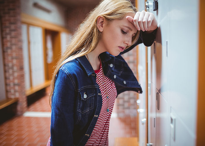 Teenage girl looking stressed and ill at school lockers illustrating patients too young to be that sick.