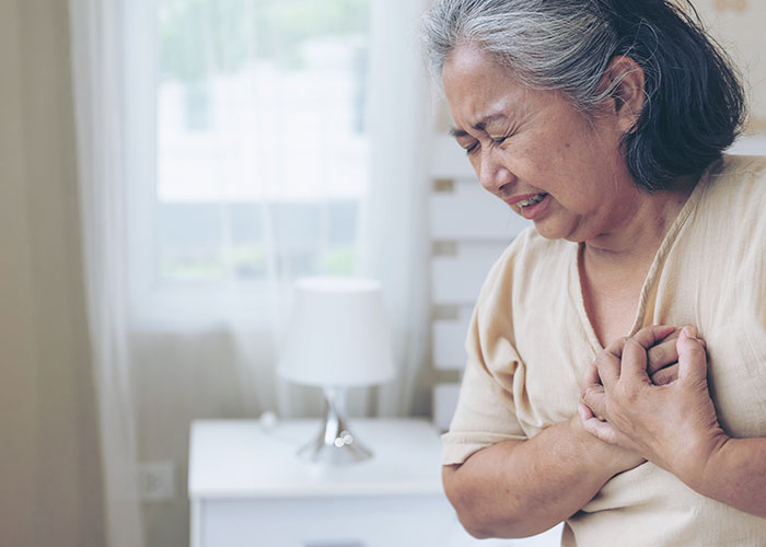 Elderly woman clutching chest in pain, highlighting cases of doctors getting it wrong with serious illness.