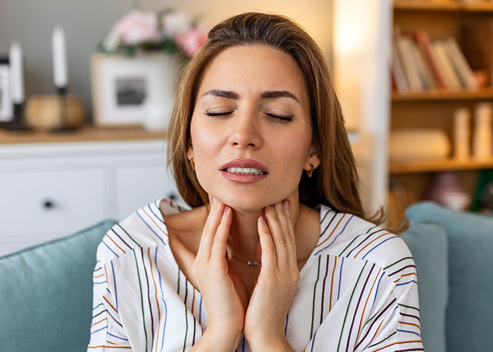 Young woman touching throat in pain, illustrating health issues and consequences of doctors getting it wrong.