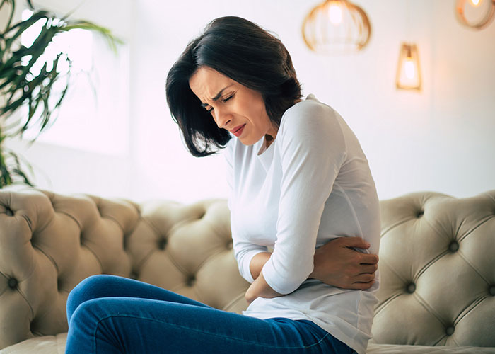 Young woman sitting on a sofa holding her stomach in pain, illustrating cases when doctors got diagnosis wrong.