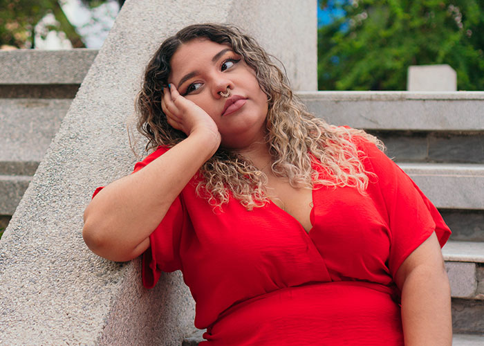 Young woman in red dress looking thoughtful while sitting on outdoor steps, reflecting on doctors getting it wrong.