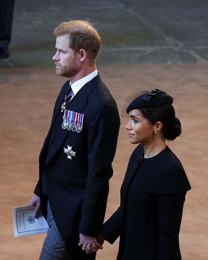 Prince Harry and Meghan Markle in formal attire holding hands at a solemn event related to Queen Elizabeth’s passing. Prince Harry and Meghan Markle in formal attire holding hands at a solemn event related to Queen Elizabeth’s passing.