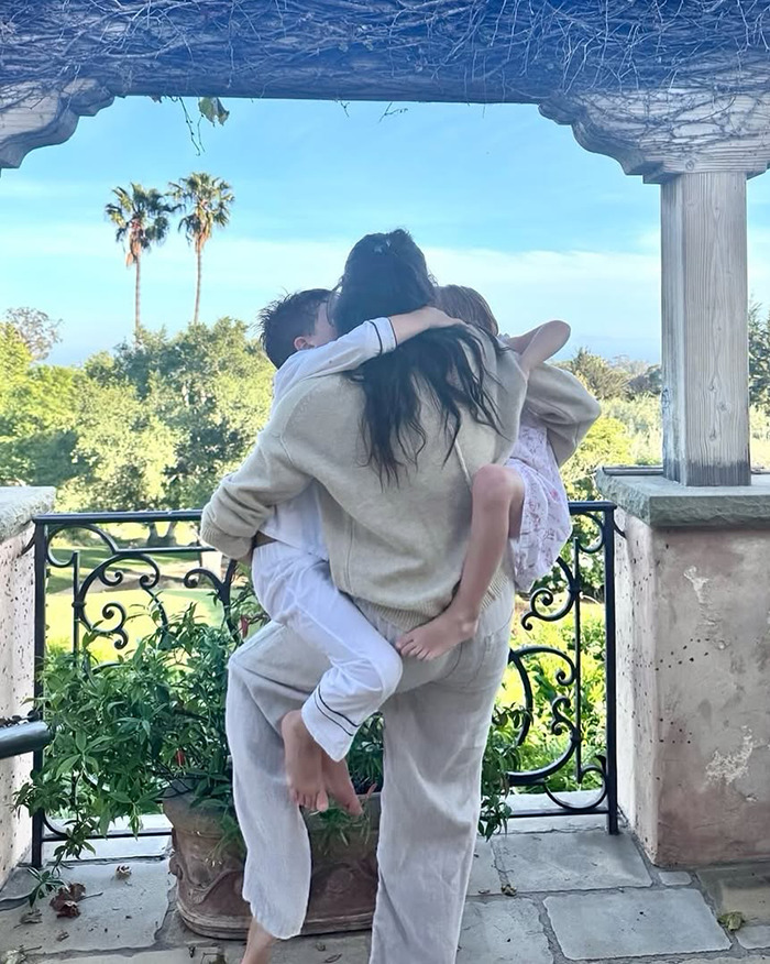 Meghan Markle embracing two children on a balcony with greenery and palm trees in background reflecting emotional moment. Meghan Markle embracing two children on a balcony with greenery and palm trees in background reflecting emotional moment.
