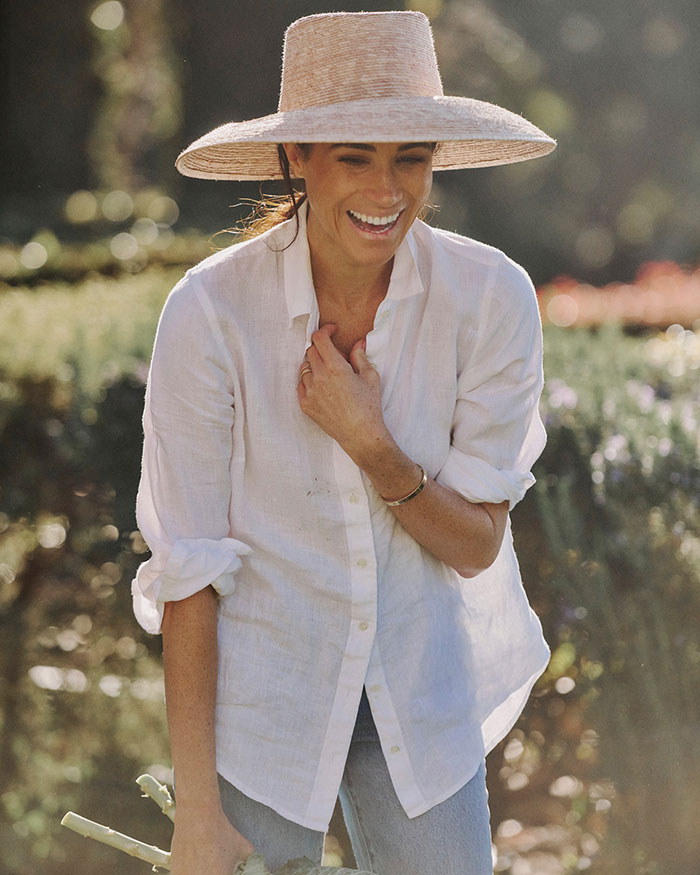 Meghan Markle in a white shirt and wide-brim hat, smiling outdoors while addressing cooking show accusations. - 13