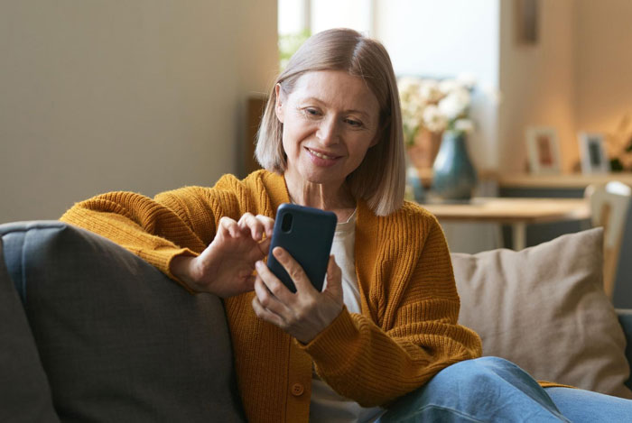 Middle-aged woman in an orange sweater using smartphone, relating to not moving on after MIL live streamed issue. Middle-aged woman in an orange sweater using smartphone, relating to not moving on after MIL live streamed issue.