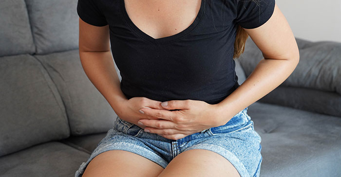 Woman sitting on a couch in casual clothes holding her stomach, depicting symptoms related to poisoning concerns.