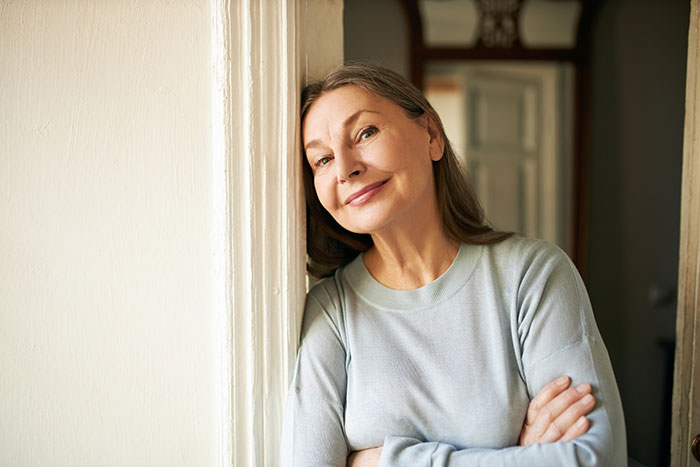 Middle-aged woman leaning against a wall with arms crossed, hinting at a story about poisoning and family conflict.