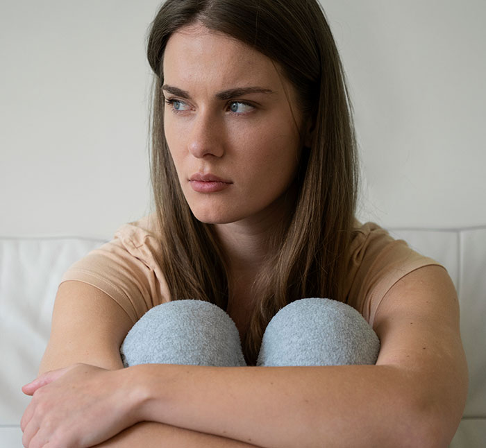 Young woman looking concerned and distant, sitting with knees hugged, reflecting tension related to poisoning and family conflict.