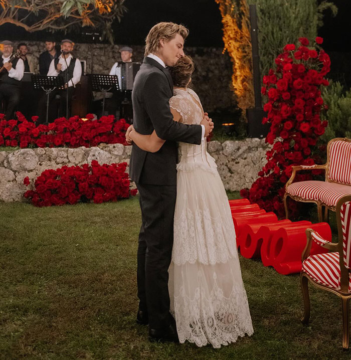 Couple embracing at a romantic outdoor event with red roses and live musicians creating a heartfelt atmosphere.