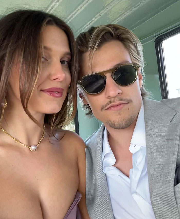 Young woman and man posing for a selfie indoors, linked to news about Millie Bobby Brown adopting a baby at 21.