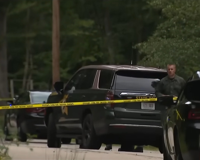 Police officer standing near black SUVs behind yellow crime scene tape at a suburban street in a depressed mom family incident.
