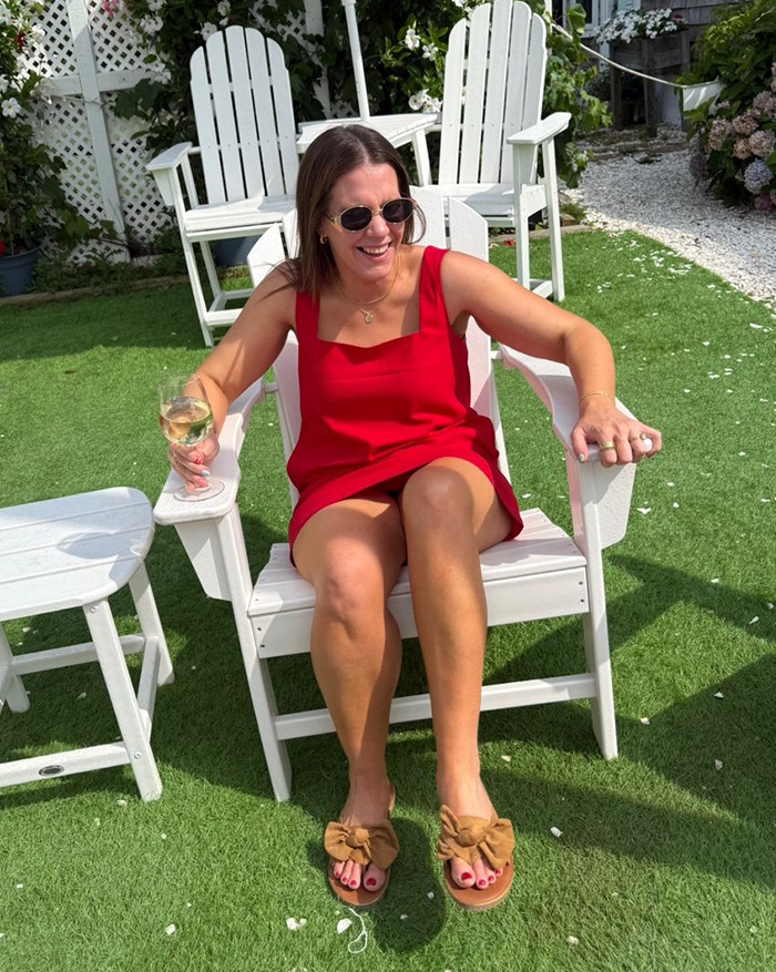 Woman in red dress sitting outdoors on white chair holding a glass, related to depressed mom and perfect family story.