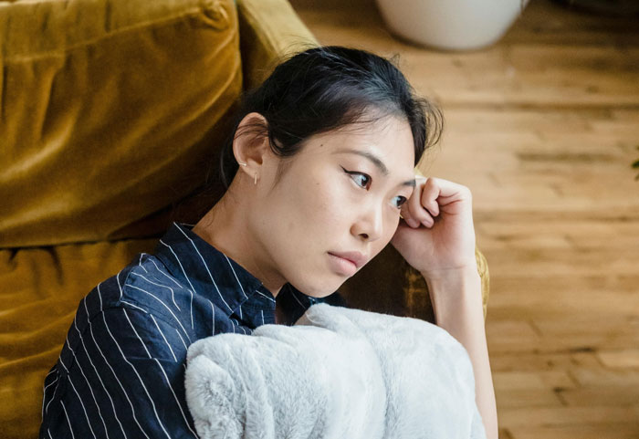 Young woman looking thoughtful and uneasy, sitting on a couch, reflecting on awkward wedding night moments. Young woman looking thoughtful and uneasy, sitting on a couch, reflecting on awkward wedding night moments.