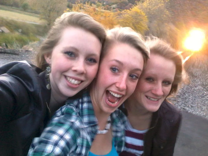 Three young women smiling for a selfie on train tracks with an oncoming train light behind them in photos taken before disaster.