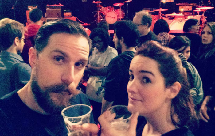 Two people holding drinks at a crowded venue, photos taken before disaster hinting at an ominous atmosphere before the event.