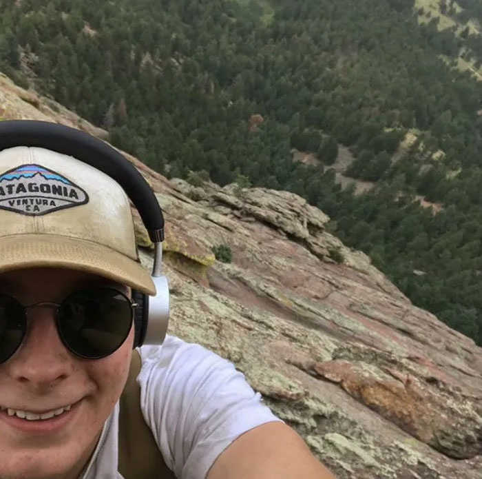 Young man wearing sunglasses and headphones taking a risky selfie on a steep rocky cliff before disaster.