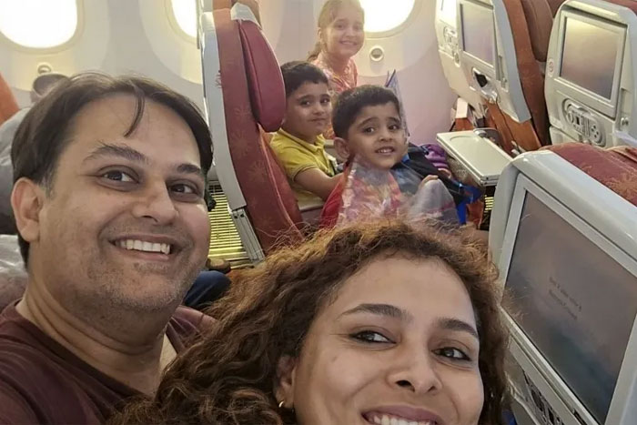 Family smiling for photos taken before disaster while seated inside an airplane cabin with children and adults.