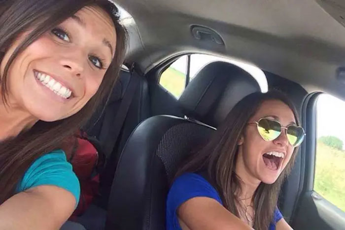 Two women taking a selfie inside a car, smiling and unaware of disaster moments before it happens.