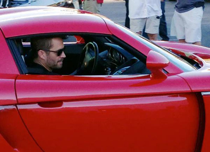 Man wearing sunglasses sitting in a red sports car in a crowd, a photo taken before disaster unfolded.