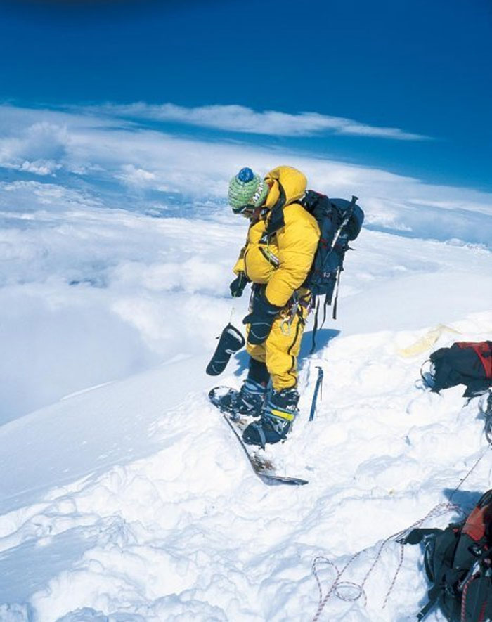 Mountaineer in yellow gear standing on snowy peak, a photo taken before disaster on an icy mountain slope.