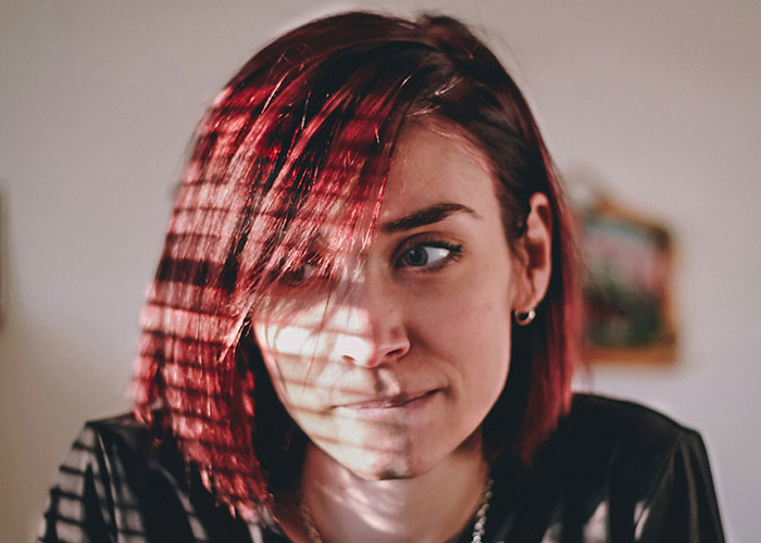 Young woman with red hair and thoughtful expression, with light patterns on her face illustrating mind tricks that actually work - 12
