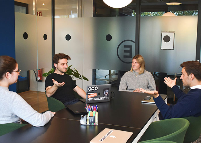 Four colleagues in a modern office having a discussion, illustrating teamwork and mind tricks that actually work. - 33