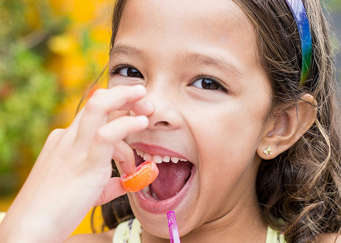 Young girl enjoying a bright orange candy, smiling widely while demonstrating mind tricks that actually work. - 17