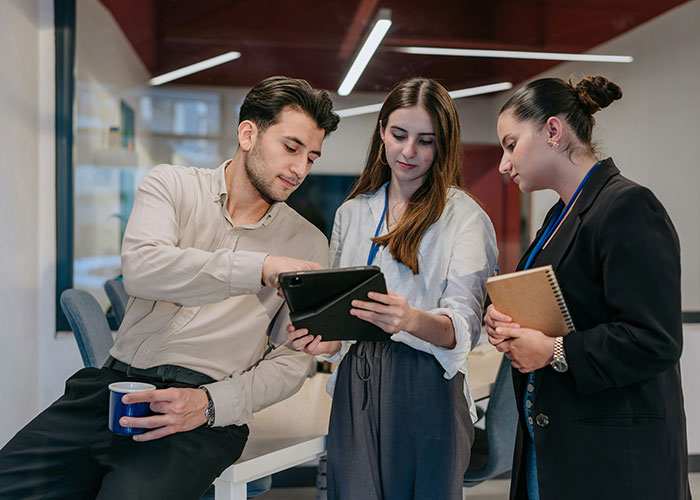 Three colleagues discussing mind tricks and strategies using a tablet in a modern office meeting space. - 9