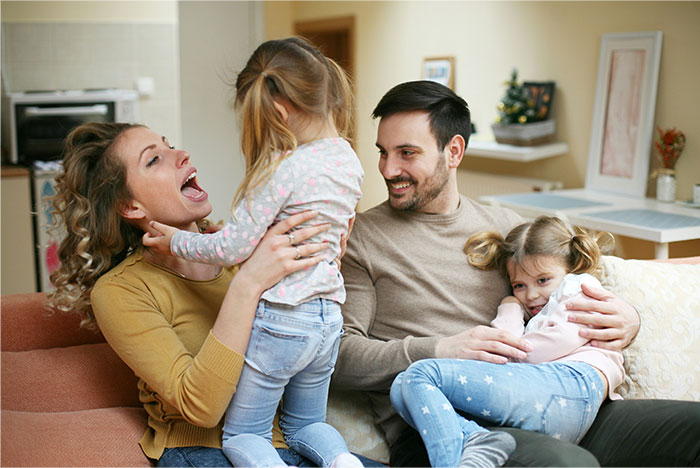 Family moment with mom showing love to girly daughter while dad holds the other child in a cozy home setting.