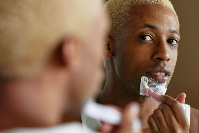 Man with blonde hair shaving in front of a mirror, reflecting on job interview red flags in a toxic workplace.