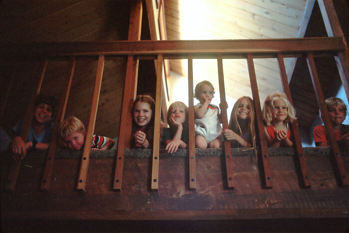 Group of children leaning on wooden railing inside a cabin, evoking hidden families and secrets discovered after someone passed.
