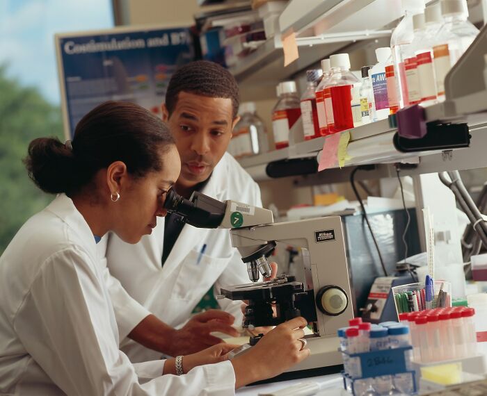 Two scientists in a lab examining samples under a microscope highlighting good news in medical research.