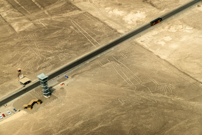 Aerial view of ancient geoglyphs in desert landscape with a road and observation tower, highlighting AI geoglyph discoveries.