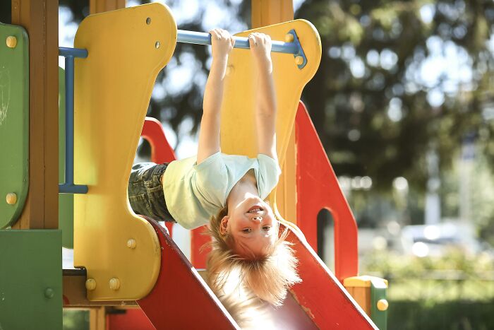 Child happily playing on colorful playhouse slide outdoors under sunlight in a neighborhood setting.