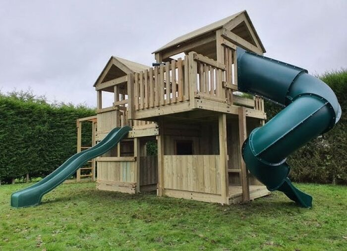 Large wooden playhouse with green slides in a backyard, highlighting privacy concerns and frustration.