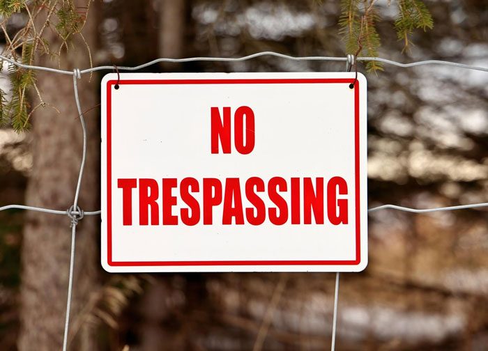 No trespassing sign posted on wire fence with blurred trees in background, illustrating nasty neighbor dispute.