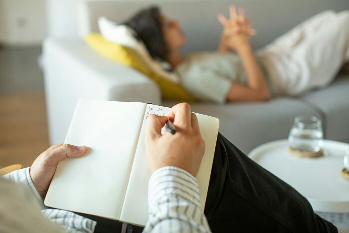 Therapist taking notes during a session with a woman lying on a couch, highlighting obsession and controversy themes.