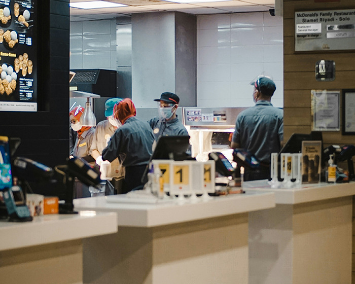 McDonald's staff working behind the counter wearing uniforms and masks in a fast food restaurant setting.